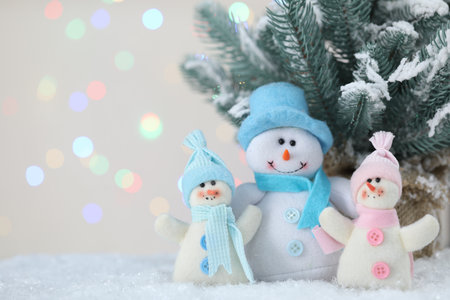 Cute snowmen and fir branches against beige background with blurred lights, bokeh effect. Space for textの写真素材