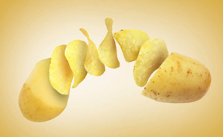 Raw potato turning into tasty crispy chips in air on yellow gradient backgroundの写真素材