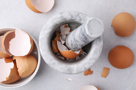 Broken eggshells, mortar and pestle on gray table, flat lay