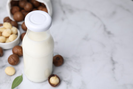 Glass bottle with macadamia milk and nuts on white table, closeup. Space for textの写真素材