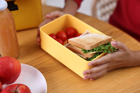 Girl with lunch box of healthy food at wooden table in kitchen, closeupの写真素材