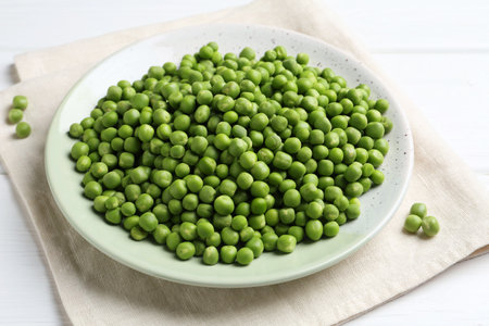 Fresh green peas in plate on white wooden tableの写真素材