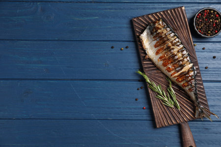 Board with delicious grilled mackerel, peppercorns and rosemary on blue wooden table, flat lay....