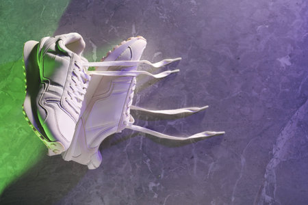Pair of stylish sneakers against marble background in neon lights, above view. Space for text