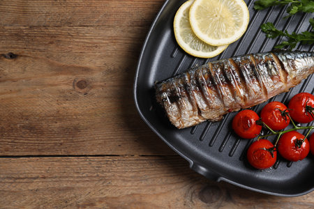 Delicious grilled mackerel, tomatoes, lemon and parsley in pan on wooden table, top view. Space for textの写真素材