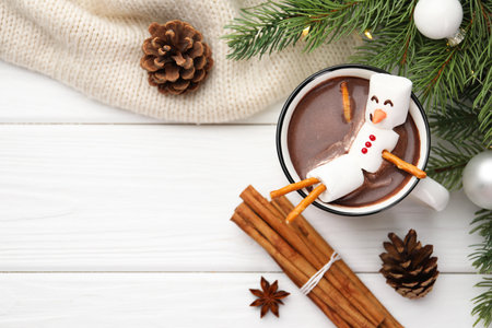 Funny snowman made with marshmallows in cup of hot chocolate and winter decor on white table, flat...