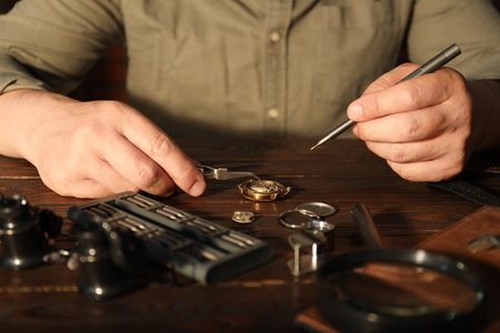 Man fixing mechanism of vintage wrist watch at wooden table, closeup