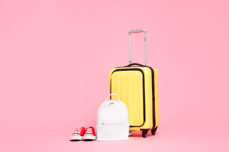Yellow suitcase, sneakers and backpack on pink backgroundの写真素材