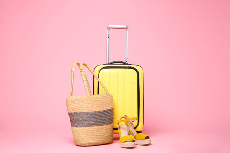 Yellow suitcase, wicker bag and shoes on pink backgroundの写真素材