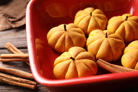Baking tray with tasty pumpkin shaped buns and cinnamon sticks on wooden table, closeup