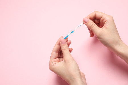 Woman holding pregnancy test on pink background, closeup. Space for textの写真素材