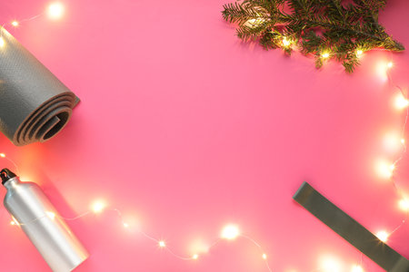 Yoga mat, band, bottle and Christmas decor on pink background, flat lay. Space for textの写真素材