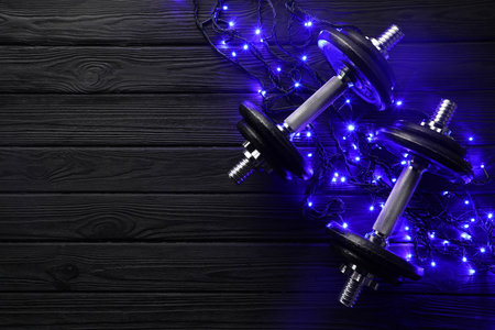 Dumbbells and Christmas lights on wooden table, flat lay. Space for textの写真素材