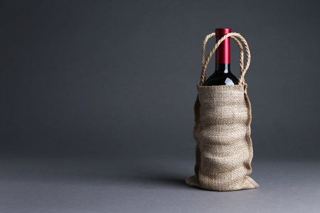 Wine bottle in burlap bag on gray background, space for textの写真素材