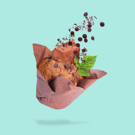 Yummy muffin and chocolate chips in air on turquoise background