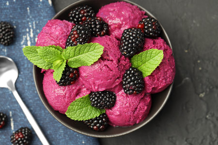 Delicious blackberry sorbet with fresh berries in bowl and spoon on gray textured table, flat lay