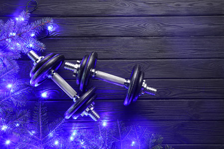 Dumbbells, fir tree branches and Christmas lights on wooden table, flat lay. Space for textの写真素材