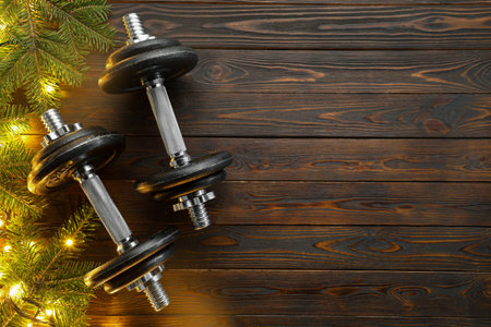 Dumbbells, fir tree branches and Christmas lights on wooden table, flat lay. Space for textの写真素材