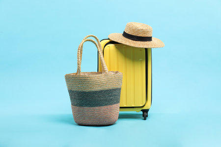 Yellow suitcase with wicker hat and bag on light blue background