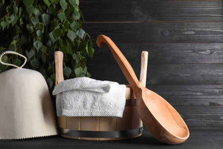 Sauna equipment. Felt wool hat, wooden bucket, towel and ladle on black tableの写真素材