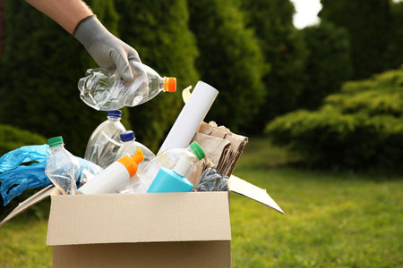 Recycling. Man putting plastic bottle into cardboard box outdoors, closeup. Space for text