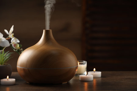 Aroma oil diffuser, burning candles and houseplants on wooden table, space for textの写真素材