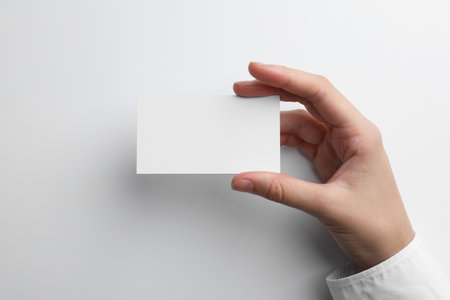 Woman with blank business card on light gray background, closeup. Mockup for designの写真素材