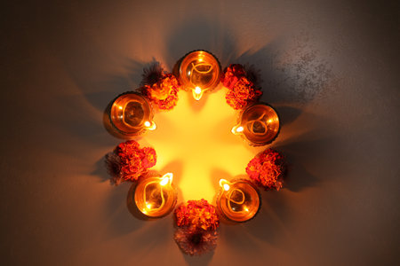 Diwali celebration. Diya lamps and beautiful flowers on dark textured surface, flat lay. Space for...