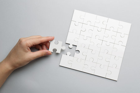 Woman solving white puzzle on light gray background, top viewの写真素材
