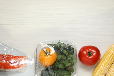 Different products with plastic food wrap on white wooden table, flat lay. Space for textの写真素材