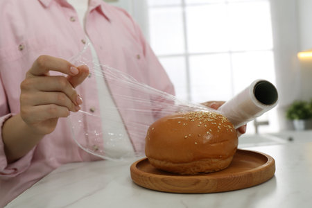 Woman putting plastic food wrap over fresh bun at white marble table in kitchen, closeupの写真素材