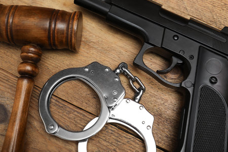 Gun, judge's gavel and handcuffs on wooden table, flat layの写真素材