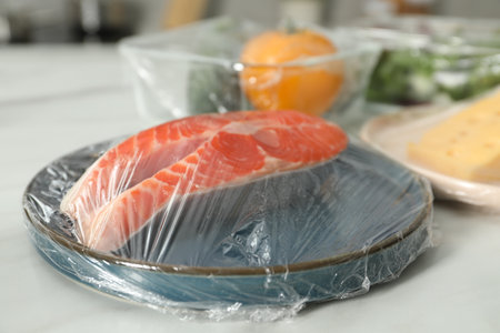 Plate of salmon with plastic food wrap on white table, closeupの写真素材