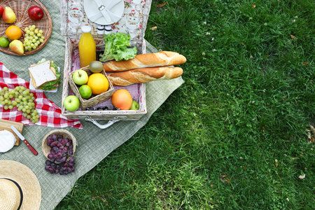 Picnic wicker basket with delicious food and drink on blanket outdoors, top view. Space for textの写真素材