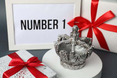 Crown, frame with phrase Number 1 and gift boxes on gray table, closeup