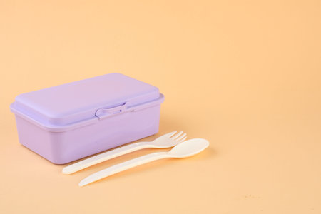 Plastic lunch box with cutlery on peach background. Space for textの写真素材