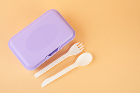 Plastic lunch box with cutlery on peach background, top view. Space for textの写真素材