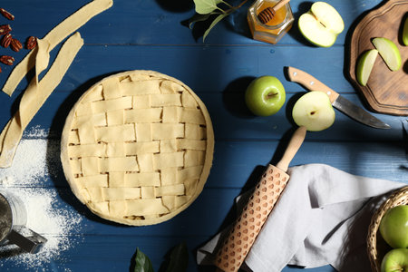Uncooked homemade apple pie and ingredients on blue wooden table, flat layの写真素材