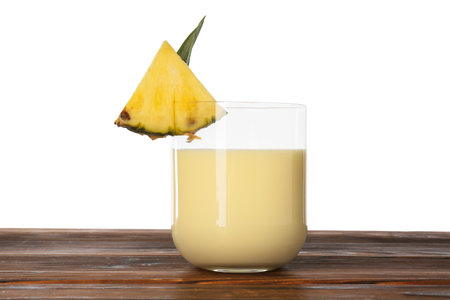 Tasty pineapple smoothie in glass and slice of fruit on wooden table against white background