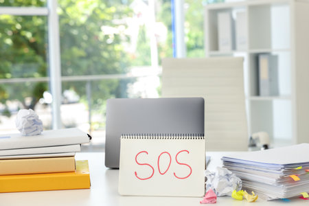 Notebook with word SOS, stationery and laptop on table in office