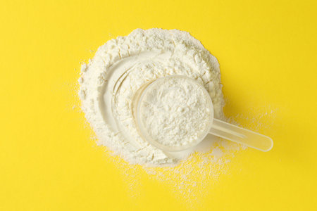 Protein powder and scoop on yellow background, top viewの写真素材