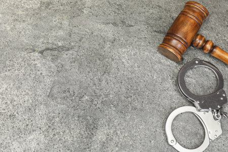 Judge's gavel and handcuffs on gray textured table, flat lay. Space for textの写真素材