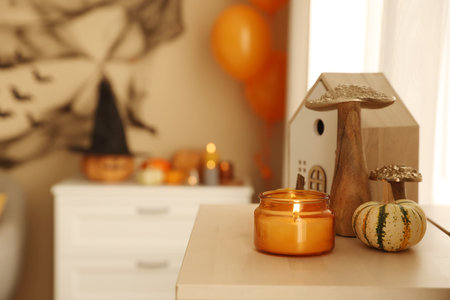 Halloween celebration. Festive decor and burning candle on chest of drawers indoors, space for textの写真素材