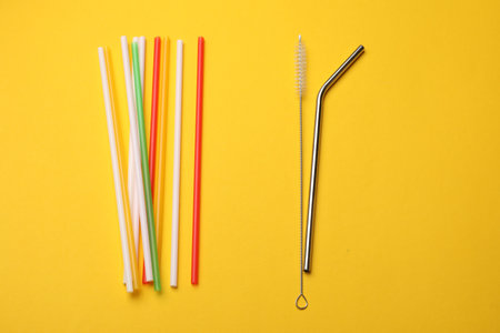 Different drinking straws and cleaning brush on yellow background, flat lay