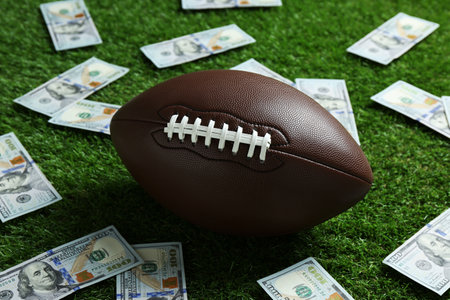 American football ball and dollar banknotes on green grass outdoorsの写真素材