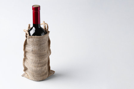 Wine bottle in burlap bag on light gray background, space for textの写真素材