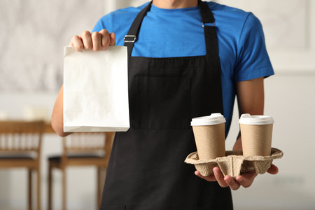 Fast-food worker with paper bag and cups indoors, closeupの写真素材