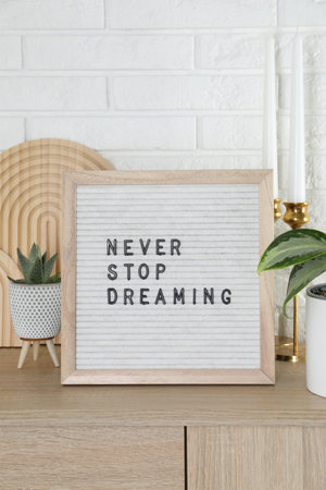 Letter board with phrase Never Stop Dreaming, plants and candles on wooden side table near white brick wallの写真素材