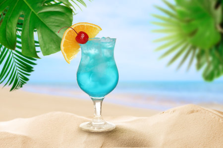 Summer beach with delicious Blue Lagoon cocktail, tropical leaves and golden sandの写真素材