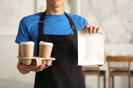 Fast-food worker with paper bag and cups indoors, closeupの写真素材